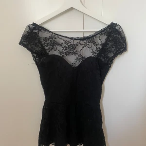 Peplumtopp/blus - Elegant svart blus/peplum från Gina Tricot med  spetsdetalj och blommigt mönster. Köpt second hand och är i använt skick men inte defekter förutom lite trådar som hänger ut.