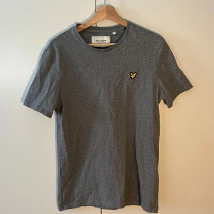 Grå t-shirt från Lyle & Scott - Säljer en stilren grå t-shirt från Lyle & Scott med korta ärmar och en liten broderad logga på bröstet. Perfekt för en avslappnad look. Använd endast en gång. Säljer då den inte passar längre. Nypris: 399, Mitt pris: 99. Skicka gärna ett meddelande vid frågor eller intresse!