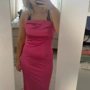 Rosa klänning från Nelly - Snygg rosa klänning från Nelly med axelbandslös design. Perfekt för festliga tillfällen. Klänningen har en smickrande passform och är gjord i ett glansigt material.