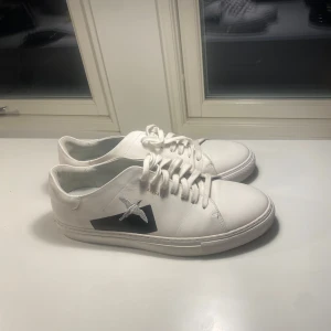 Axel Arigato skor  - Snygga vita sneakers från Axel Arigato med en svart detalj på sidan och snörning framtill. Perfekta för en stilren look. Dessa har bara användts 2 gånger då dessa är fel storlek så skicket är 9.5/10. Säljs nu eftersom jag letar ett par nya skor. Nypris 2600kr.