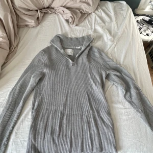Grå ribbad tröja från Jack & Jones - Säljer en stilren grå ribbad tröja från Jack & Jones som jag använt väldigt lite. Tröjan har en dragkedja vid halsen och långa ärmar, perfekt för en avslappnad look. Passar bra till både jeans och chinos. Nypris 699kr!