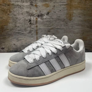 Adidas Campus (nyskick) - Snygga gråa Adidas Campus sneakers i mocka med de klassiska vita tre ränderna på sidan. Skorna är i extremt bra skick och bara använda ett par gånger. Nypris: 1400kr, vårt pris: 749kr.        Storlek 43,5. Dessa skor kommer ge din stil ett lyft💯(pris kan diskuteras)