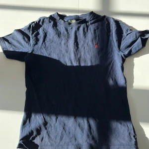 Mörkblå t-shirt från Ralph Lauren - Säljer en klassisk mörkblå t-shirt från Ralph Lauren med korta ärmar. Den har en broderad röd logotyp på bröstet. Perfekt för en stilren och avslappnad look. Storlek 175 cm. Bra skick!