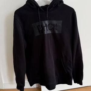 Svart hoodie från DirtCult - Säljer en svart hoodie från DirtCult med en stor logga på bröstet. Tröjan har en klassisk design med huva och dragsko samt en stor magficka framtill. Perfekt för en avslappnad stil.
