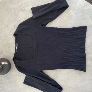 Svart ribbad tröja från Bik Bok - Säljer en stilren svart ribbad tröja från Bik Bok. Tröjan har en fyrkantig halsringning och trekvartsärmar, vilket ger en modern look. Perfekt för att matcha med olika outfits. 
