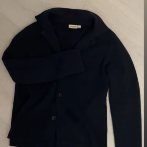 Mörkblå cardigan från Kappahl - Säljer en stilren mörkblå cardigan/overshirt från Kappahl. Långa ärmar och knappar framtill. Perfekt för en elegant och avslappnad look.