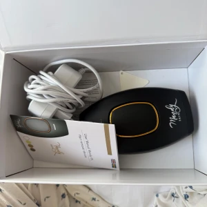 Mandy Skin IPL Hårborttagningsenhet - Säljer en IPL hårborttagningsenhet från Mandy Skin. Enheten är svart med gulddetaljer och kommer med en strömadapter. Perfekt för smidig och effektiv hårborttagning hemma.