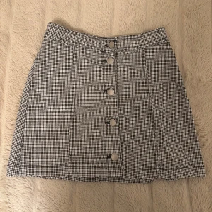 Svartvit rutig kjol med knappar, H&M - Snygg svartvit rutig kjol med knappar upptill. Kjolen har en klassisk A-linjeform och är lätt att matcha med olika toppar.