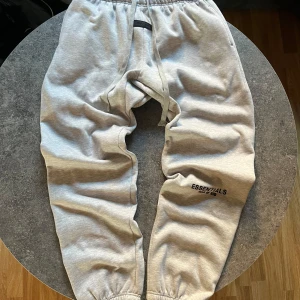 Grå mjukisbyxor från Essentials - Säljer ett par grå mjukisbyxor från Essentials med elastisk midja och muddar vid bensluten. Byxorna har en diskret logga på benet och en bakficka. Perfekta för en avslappnad stil. Storlek XL men sitter som M/L