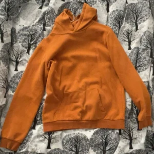 Orange hoodie - Säljer en snygg orange hoodie med en stor ficka framtill. Perfekt för kyliga dagar med sin mjuka och bekväma passform. Huvan ger extra värme och stil.
