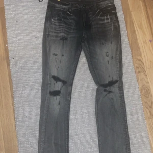 Intressekoll 01 - Snygga svarta jeans med slitningar på knäna och en cool tvättad look. De har en klassisk femficksdesign och stängs med dragkedja och knapp. Perfekta för en avslappnad stil.