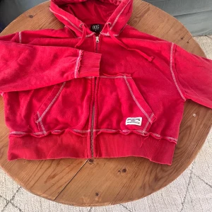 Röd hoodie från Urban Outfitter - Säljer en cool röd hoodie från Urban Outfitters med dragkedja och huva. Den har en avslappnad passform och ribbade muddar. 