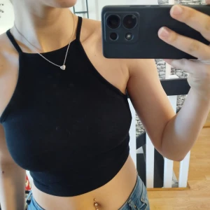 Svart ärmlös croppad topp - Snygg svart ärmlös croppad topp med smala axelband. Perfekt för varma dagar eller som en del av en lager-på-lager look. Enkel och stilren design som passar till det mesta.