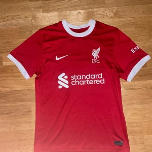 Röd fotbollströja från Nike - Säljer en röd fotbollströja från Nike med vit krage och vita detaljer på ärmarna. Tröjan har korta ärmar och är tillverkad i Dri-FIT-material för optimal komfort. Perfekt för fotbollsfans! ⚽