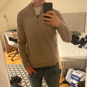 Beige halfzip från Stenströms - Säljer en stilren beige tröja från Stenströms med dragkedja vid halsen. Tröjan har långa ärmar och en ribbad krage. Perfekt för en avslappnad men ändå elegant look. Den är perfekt med skjorta under.