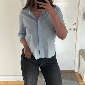 Ljusblå skjorta - Zara - Stilren och luftig ljusblå skjorta från Zara. Modellen har trekvartsärmar, dold knäppning framtill och en lätt, rak passform som ger en avslappnad men elegant look. Perfekt både till vardags och jobb, kan bäras instoppad i jeans eller löst över kjol/byxor. Har små fläckar på framsidan som inte syns i helheten (se sista bild).