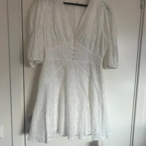 Vit blommig kortklänning från Adoore - HELT NY Supersöt vit klänning från Adoore med broderade blommor, puffiga kortärmar och v-ringad hals. . Perfekt för sommaren och studenten.