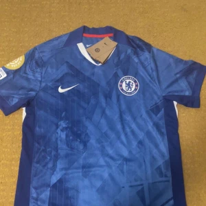 Chelsea FC Palmer 10 Nike fotbollströja M - Chelsea FC matchtröja med Palmer 10 på ryggen. Snyggt blått geometriskt mönster, vita detaljer och klubbmärke på bröstet. Tillverkad i Dri-FIT material som andas och håller dig torr. Kortärmad och med Nike-logga på framsidan.