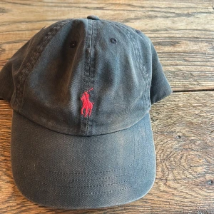 Svart keps från Polo Ralph Lauren - Klassisk svart keps från Polo Ralph Lauren med röd broderad logga, den är typ brun Vene hur jag ska säga men den är rätt så använt värt för pengarna 