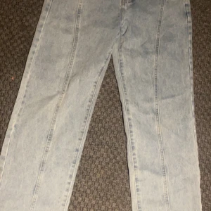 Ljusblå raka jeans med söm-detaljer - Säljer ett par ljusblå jeans med raka ben och markerade sömmar längs framsidan. Jeansen är tillverkade i en mix av bomull, polyester och viskos för en skön känsla. Perfekta för dig som gillar en clean och stilren look.
