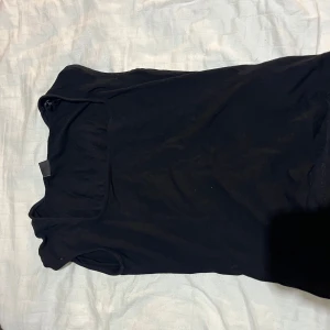 Svart ärmlös topp från Gina Tricot - En svart, enkel och stilren ärmlös topp från Gina Tricot. Toppen har rundad halsringning och är gjord i mjuk bomull, perfekt att matcha med jeans eller kjol för en clean look.