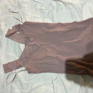 Rosa ribbad linnetopp med spets - Supersöt ljusrosa linnetopp från Mywear med breda spetsband och ribbad struktur. Djup v-ringning med dekorativ spets runt halsen och axelband. Perfekt att styla med jeans eller kjol för en trendig look.