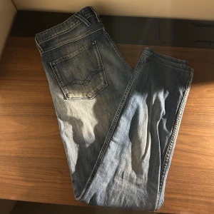Replay Anbass ljusblå jeans - Säljer ett par Replay Anbass jeans i ljusblå tvätt med snygga slitningar och klassiska femficksdetaljer. Jeansen har raka ben och normal passform, med Replay-logga på bakfickan och läderpatch i midjan. Perfekta för en avslappnad och trendig look.