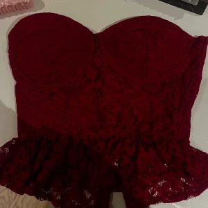 Vinröd spetskorsett från Bik Bok - Supersnygg vinröd korsett från Bik Bok i spets med volangkant nertill. Axelbandslös bandeau-modell med vadderade kupor och dragkedja bak. Perfekt för dig som vill sticka ut med en romantisk och trendig look.