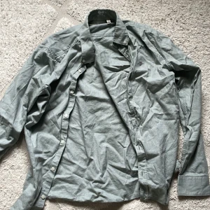 Ljusgrå bomullsskjorta från GANT - Snygg ljusgrå skjorta från GANT i bomull med klassisk krage och broderad logga på bröstet. Skjortan har långa ärmar och knäppning framtill. Perfekt för en clean och stilren look.