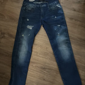Replay Hyperflex blå jeans, W29 L32 - Säljer ett par Replay Hyperflex jeans i mörkblå tvätt med slitningar och snygga detaljer. Jeansen har klassisk femficksdesign, raka ben och stretchigt material för extra komfort. Perfekta för dig som gillar en avslappnad men trendig look.