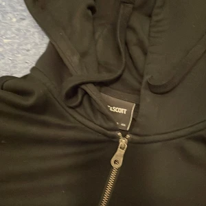 Svart hoodie från Lyle & Scott, L - Svart hoodie från Lyle & Scott med dragkedja och huva. Klassisk gul logga broderad på bröstet och två fickor framtill. Tillverkad i mjukt material, perfekt för chill dagar. Snygg och enkel design som funkar året runt.