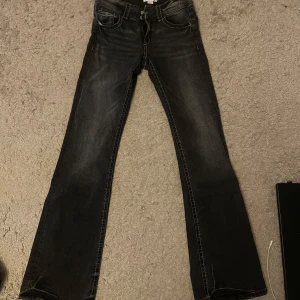 Svarta bootcut jeans med slitningar - Snygga svarta jeans med bootcut passform och lätt slitna detaljer. Jeansen har klassiska fem fickor, kontrastsömmar och dragkedjegylf. Perfekta för dig som gillar en lite vidare siluett nertill och vill ha en cool, avslappnad look.