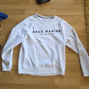 Vit sweatshirt från Race Marine M - Vit sweatshirt från Race Marine med tryck på bröstet. Klassisk rund halsringning och långa ärmar. Mjuk och skön i bomullsmix, perfekt för en clean och sportig look. Passar dig som gillar enkel stil med tydlig logga framtill.
