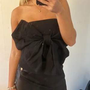 Svart axelbandslös topp med rosett - Säljer en svart axelbandslös topp med en stor rosett framtill. Toppen har en elegant och stilren look, perfekt för dig som vill sticka ut.