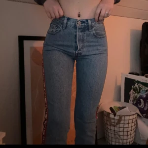 Levis jeans med logoband i sidan - Snygga ljusblå Levis jeans med medel midja och raka ben. På sidorna finns ett vitt logoband med Levis-tryck och röda samt blå detaljer. För korta i benen på mig