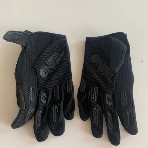 Svarta O'Neal cykel/cross handskar M - Säljer ett par svarta O'Neal handskar i storlek M. De har ventilerande mesh på ovansidan, förstärkta partier och greppvänlig insida med texten 'ENJOY THE RIDE'. Perfekta för cykling eller annan sport där du vill ha bra grepp och skydd.
