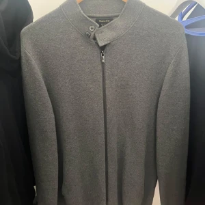 Massimo Dutti Zip up - Snygg grå kofta från Massimo Dutti i mjuk bomull. Den har en stilren ståkrage med två knappar och hel dragkedja framtill. Perfekt för lager-på-lager och passar till både jeans och chinos. Enkel, modern design som funkar året runt.
