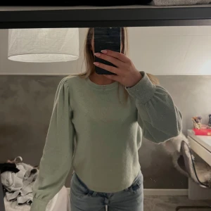 Ljusgrön stickad tröja med puffärm - Superfin ljusgrön stickad tröja med puffiga ärmar och rund hals. Tröjan har en mjuk och mysig känsla, perfekt att matcha med jeans eller kjol. Stilren design utan mönster och med ribbade muddar vid ärmslut och hals.