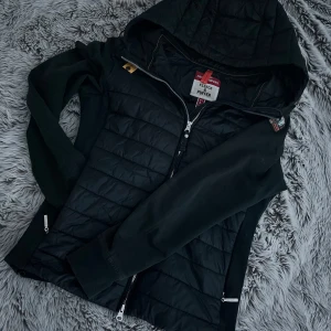 Svart parajumper cardigan  - Svart cardigan från Parajumpers i storlek L. Men passar även M då den är liten i storleken. Jackan har huva, quiltad framsida och detaljer i fleece. Snygg dragkedja framtill och märke på ärmen. Bra jacka nu inför hösten och vintern. 