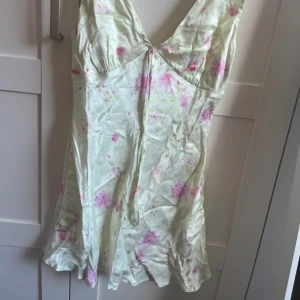 Klänning - Jättesöt klänning från ASOS DESIGN i satinliknande material med rosa blommigt mönster. Klänningen har v-ringad hals och breda axelband, samt en liten knytning framtill. Storlek S, aldrig använd🤍