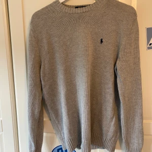 Grå stickad tröja från Polo Ralph Lauren (NY SKICK) - Säljer en klassisk grå stickad tröja från Polo Ralph Lauren med rund halsringning och broderad marinblå logga på bröstet. Inget hål eller fläckar, är i storlek m men sitter som en s. Jätte fint skick, priset ej huggen i sten. Hör bara av dig vid funderingar eller något!!