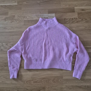 Ljusrosa stickad polotröja - Superfin ljuslila stickad polotröja med ribbad hög krage och muddar. Tröjan är croppad och har en loose passform med långa ärmar. Perfekt för dig som vill ha en mysig och trendig look till hösten eller vintern.