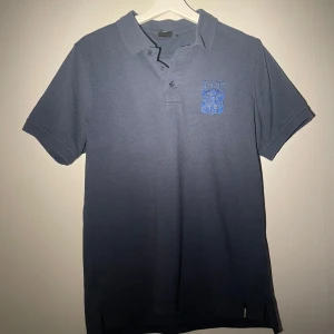 Blå IFK Göteborg piké  - Snygg mörkblå pikétröja från Craft med IFK Göteborgs broderade klubbmärke på bröstet. Klassisk krage, knappar framtill och korta ärmar. Perfekt för dig som vill visa ditt stöd för laget med stil. 