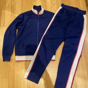 Marinblå ziptröja från Zara - Sportig marinblå ziptröja från Zara med vita och röda ränder längs krage och muddar. Tröjan har hög krage, hel dragkedja och två fickor med dragkedja. Perfekt för en chill och avslappnad stil.