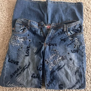 Moto Blues jeans med broderier och tryck - Unika blå jeans från Moto Blues med coola broderier, stjärnor och texttryck som 'LOVE' och 'EMOTION'. Jeansen har klassisk femficksdesign och är tillverkade i en mix av bomull, rayon, polyester och spandex för en bekväm passform.