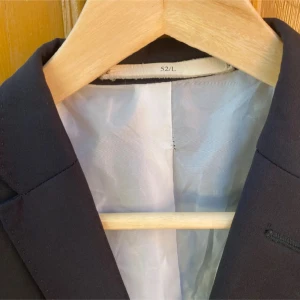 Svart kavaj storlek 52/L, - Stilren svart kavaj med klassisk passform och enkel knappstängning framtill. Kavajen har två fickor med lock och en bröstficka, samt slät design utan mönster. Fodrad insida i ljus färg. Perfekt för dig som vill ha en clean och snygg look. Sitter mer som 50