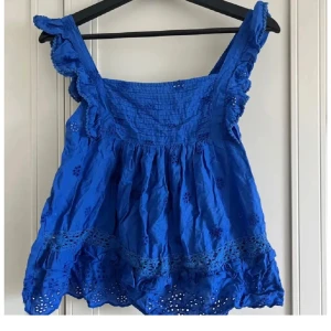 Blå broderad topp - Säljer denna super fina broderade blåa topp från mango. Har vikande på axlarna och vid magen. Litet hål vid en söm längst ner på toppen, se bild.