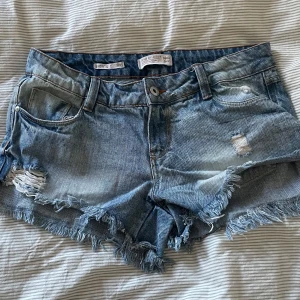 Lågmidjade jeansshorts från Nice Girl - Snygga blå jeansshorts från Nice Girl med låg midja, slitna detaljer och fransig kant. Klassisk denim med coola slitningar framtill och bakfickor. 