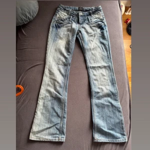 Lågmidjade jeans - Snygga blå bootcut lågmidjade jeans. Jeansen har en ljus tvätt och subtila skuggningar längs benen för en cool vintagekänsla. Perfekta för dig som gillar en avslappnad men trendig look. Har aldrig använts men saknar prislapp