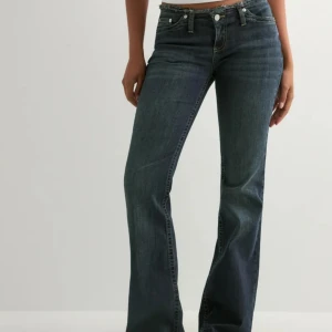 Mörkblå bootcut jeans med låg midja - Snygga mörkblå jeans med bootcut och låg midja. Klassisk femficksmodell med dragkedja och knapp framtill. Jeansen har en lätt tvättad look och raka ben som blir vidare nedtill. Perfekta för en avslappnad och trendig stil.